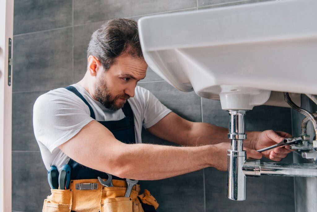 focused male plumber in working overall fixing sink in bathroom 1